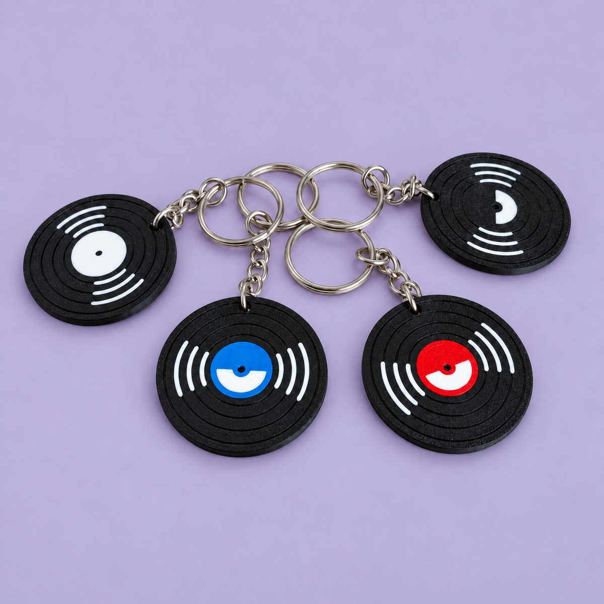 Four miniature black vinyl record NFC keychains with white, black, blue and red centres, photographed from an angle on a lavender background.