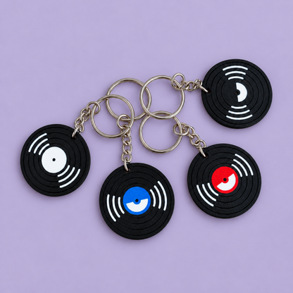 Top view of four black vinyl record NFC keychains with white, black, blue and red centres and silver keyrings on a lavender background.