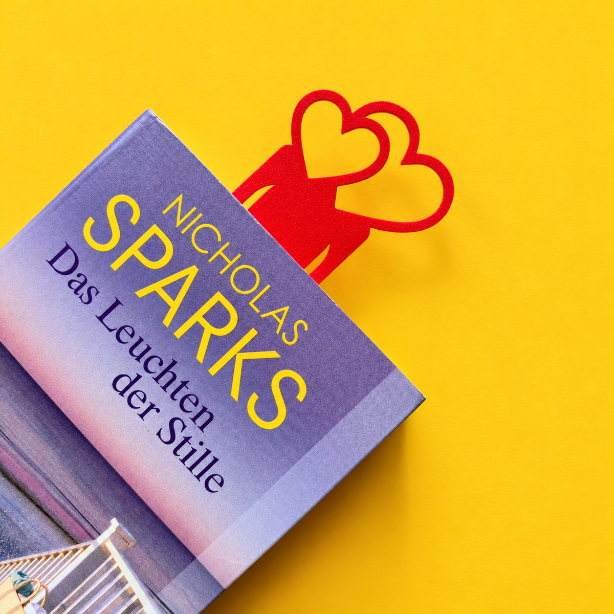 Red two-heart bookmark tucked into a closed book on a yellow background
