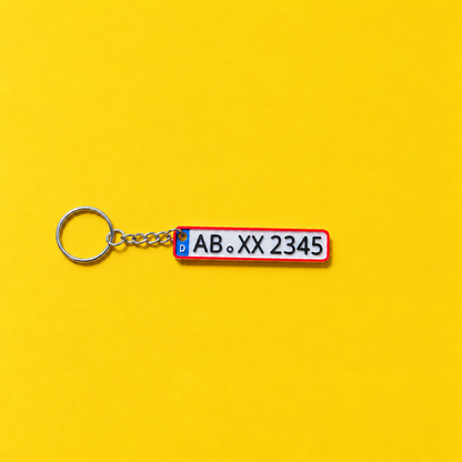 Miniature license plate keychain with black lettering and red border on a yellow background